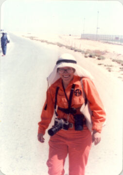 A woman in an orange jumpsuit wearing a Saudi headdress in the desert