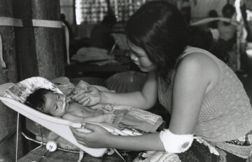 A woman feeds a baby, black and white.