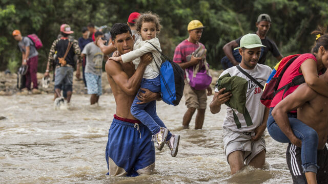 A father carries a girl across a river with a group of migrants