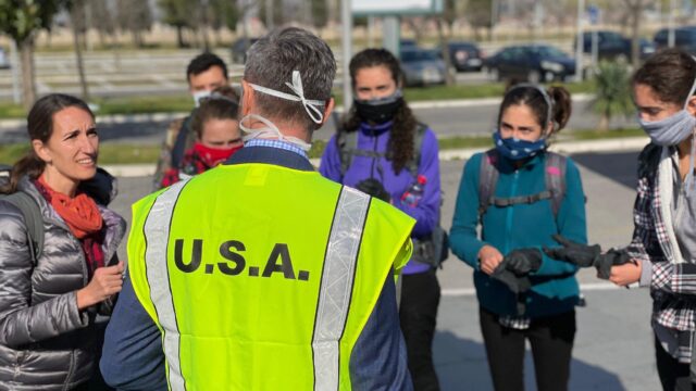 A man in a USA vest speaks to a masked group
