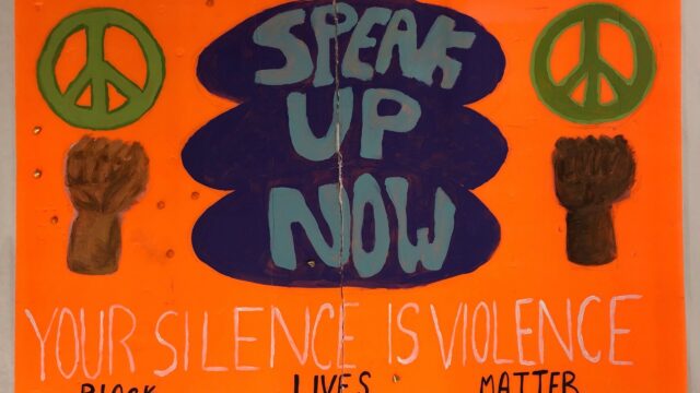 An orange poster that says Speak Up Now Your Silence is Violence