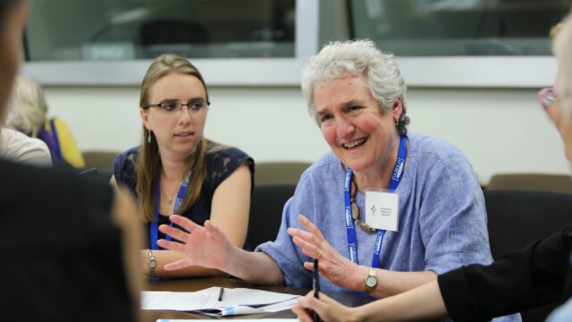 A teacher speaks from a conference table