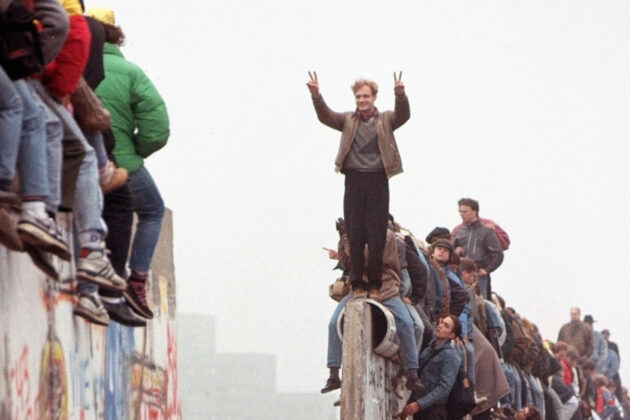 a man stands on top of the berlin wall as it is taken down