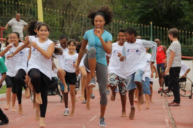 Woman practices high knees on a track with children following behind her smiling.