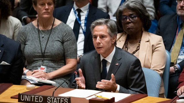 Secretary Blinken sits at a table speaking behind a placard that reads “United States” with Ambassador Thomas-Greenfield seated behind him.