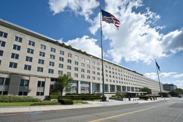 Large building with windows behind a waving American flag on a sunny day